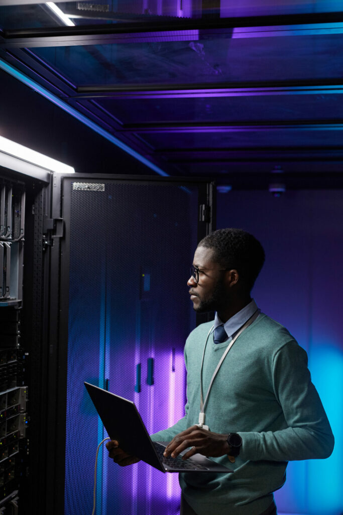 man looking at server holding laptop working at tech company