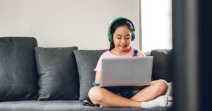 Kid sitting on a grey couch with a laptop