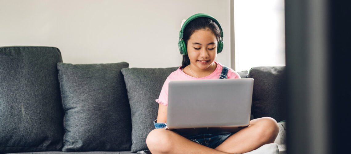 Kid sitting on a grey couch with a laptop